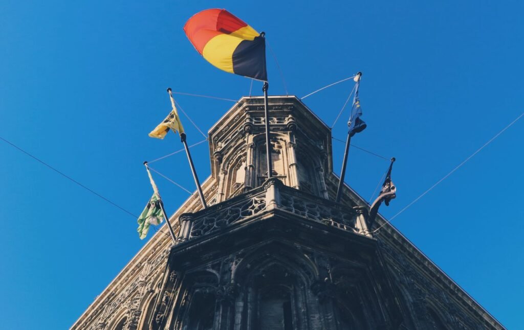 Historic building in Ghent with Belgian and regional flags against a clear blue sky.